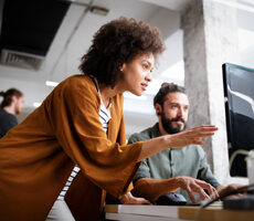A man and woman collaborating on a computer in an office, engaged in productive work.