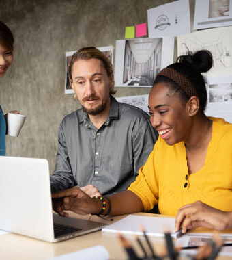 Decorative image of 3 diverse people looking at a laptop on a desk