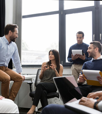 Office workspace with 4 diverse individuals sitting in discussion holding note pads.