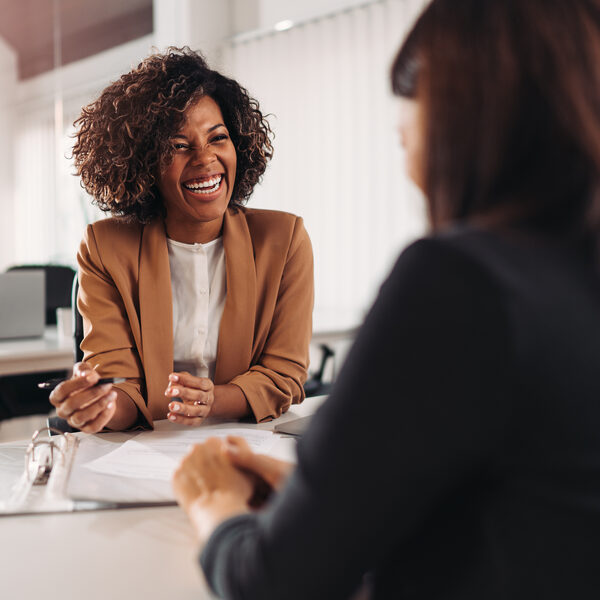 Two women sitting across a business table talking and laughing. Diverse, professional leaders and talent